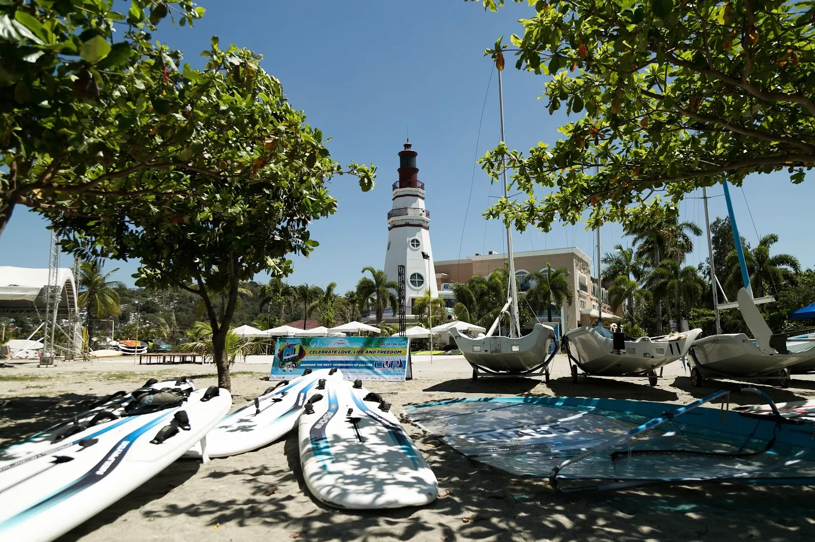 Sailing equipment stored under the trees, lighthouse behind