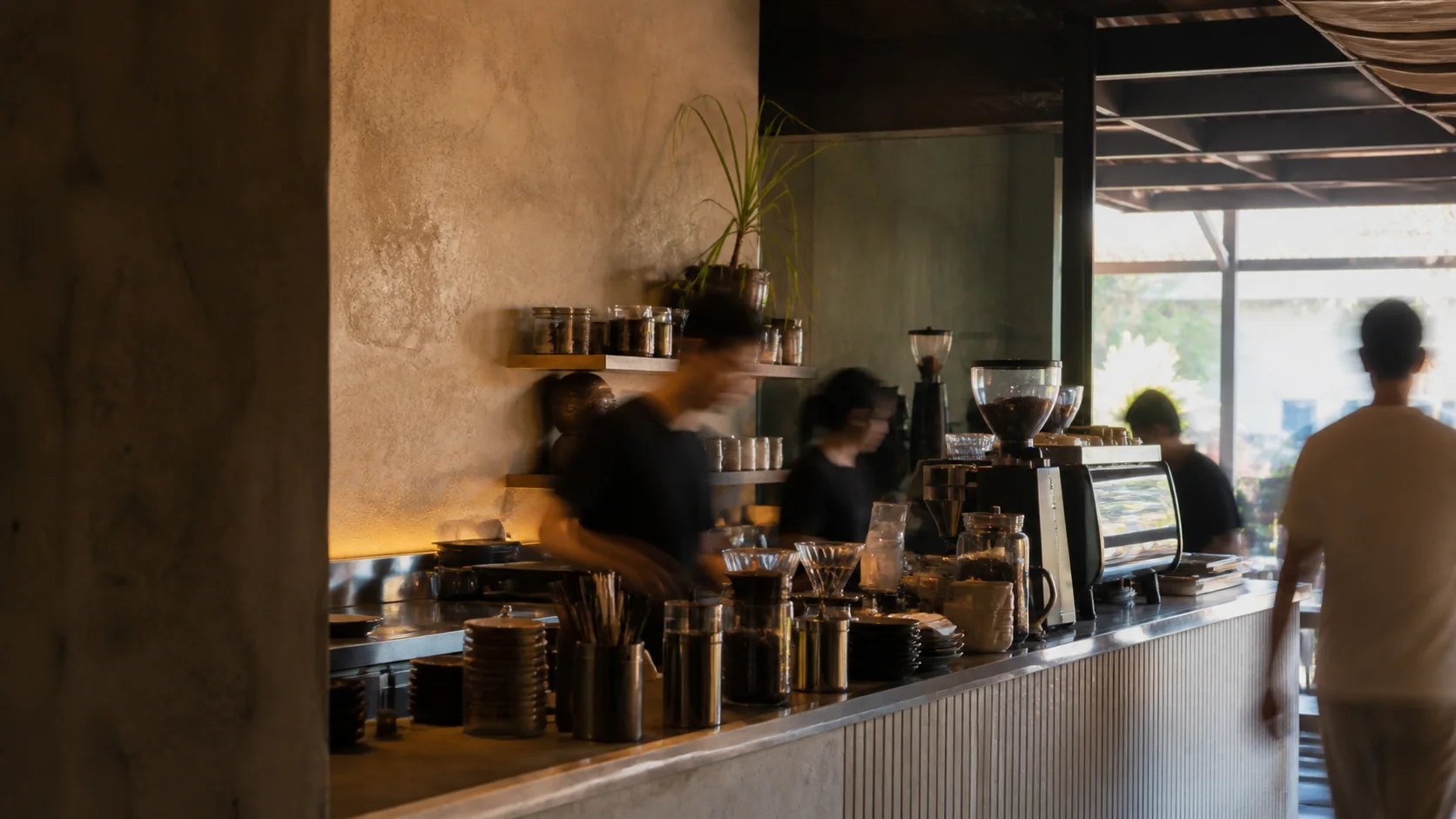 Cafe staff move behind a warm stone counter, their figures softened by motion blur.