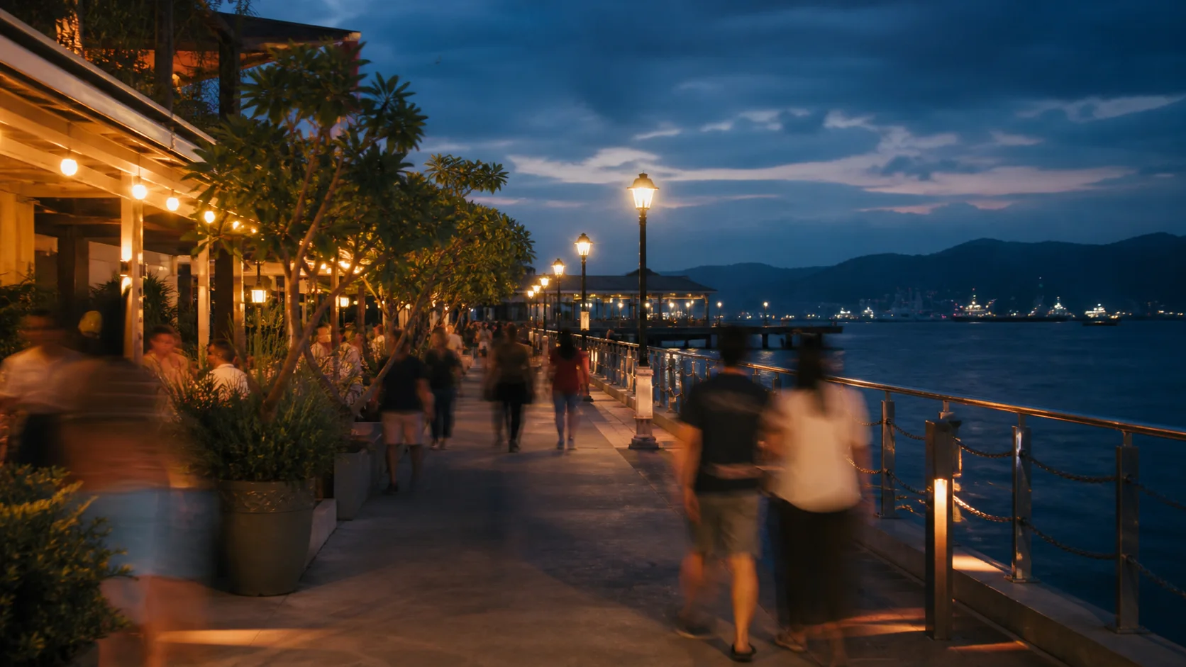 People strolling the Subic Bay waterfront at blue hour, softened by motion blur.